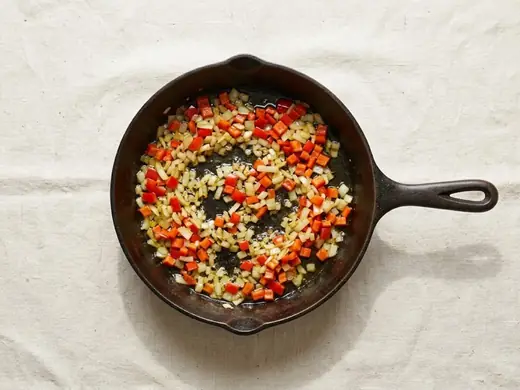Onion and red pepper softening in a cast-iron skillet